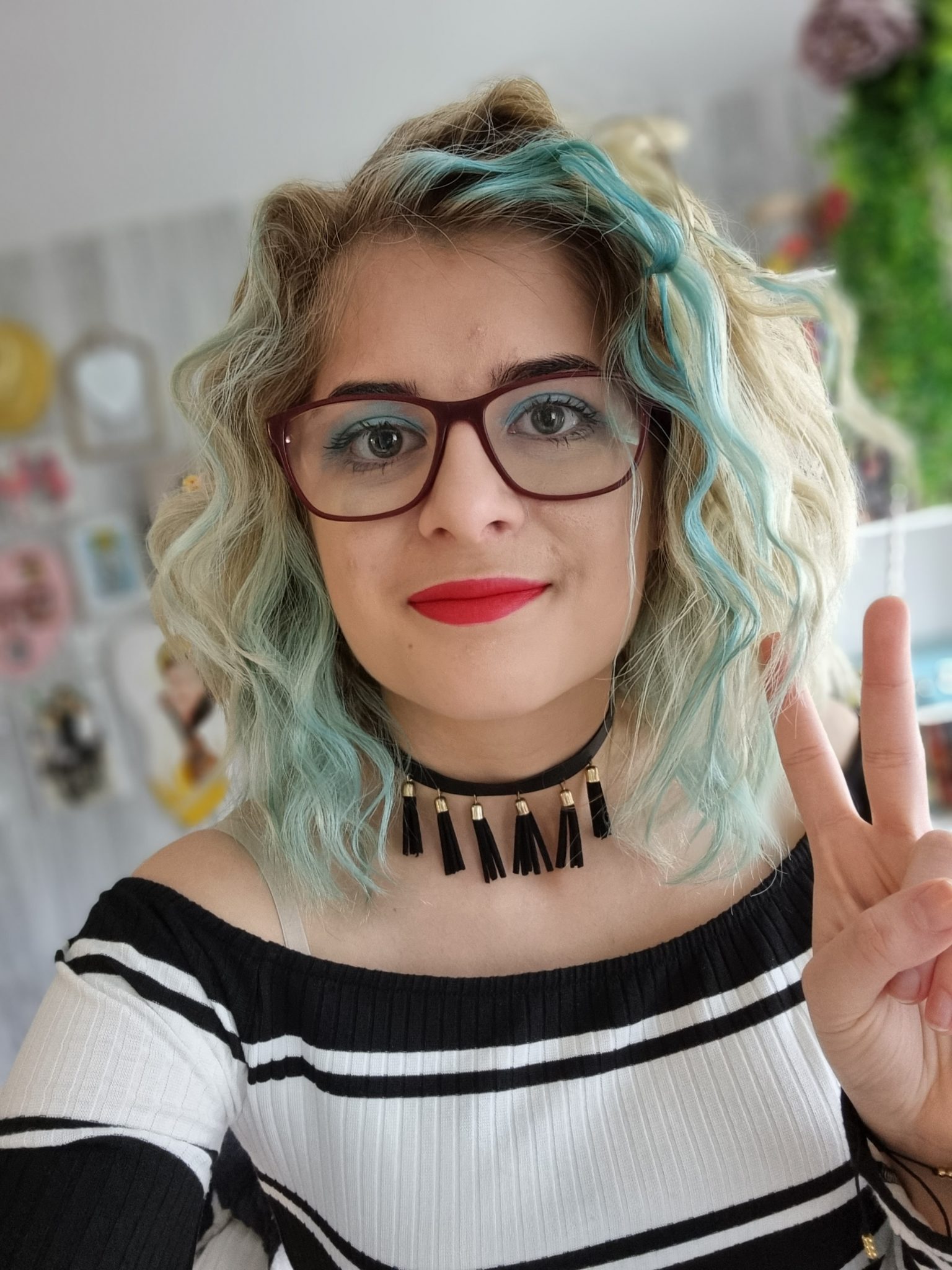 This is Weronika, she's wearing a black and white striped top with a black tassled necklace, she has glasses and shoulder length blond and blue curly hair. 