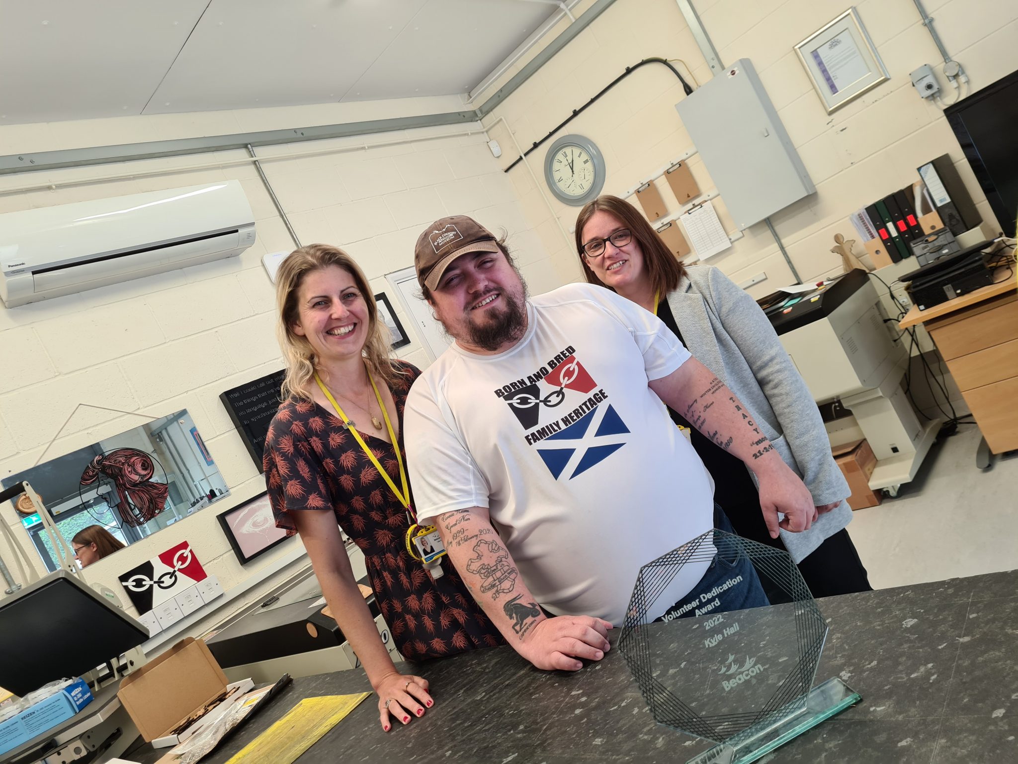 Here's our chief executive Lisa on the left, volunteer Kyle in the middle and Debbie our People Manager on the right. They are stood in our Fab Lab and on the worktop in front of Kyle is his award, made of glass and hexagon shape.